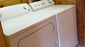 A laundry room with a front-loading washer and dryer, wooden walls, and a tiled floor. - RIVERVIEW ADIRONDACK RUSTIC APARTMENT (Warrensburg)