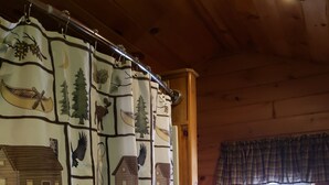 A wooden cabin interior with a cabin-themed shower curtain, a wooden dresser, and a window with blinds. - RIVERVIEW ADIRONDACK RUSTIC APARTMENT (Warrensburg)