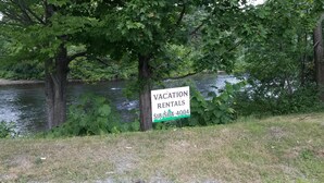 A sign for vacation rentals by a river with a contact number. - RIVERVIEW ADIRONDACK RUSTIC APARTMENT (Warrensburg)