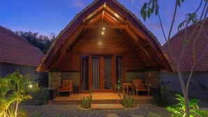A wooden cabin with a pitched roof, a front porch with seating, and a gravel pathway. - Tahoma Villas Labuan Bajo by ABM (Labuan Bajo)