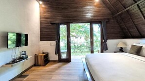 A bedroom with a large bed, a TV mounted on the wall, a wooden ceiling, and a view of greenery outside. - Tahoma Villas Labuan Bajo by ABM (Labuan Bajo)