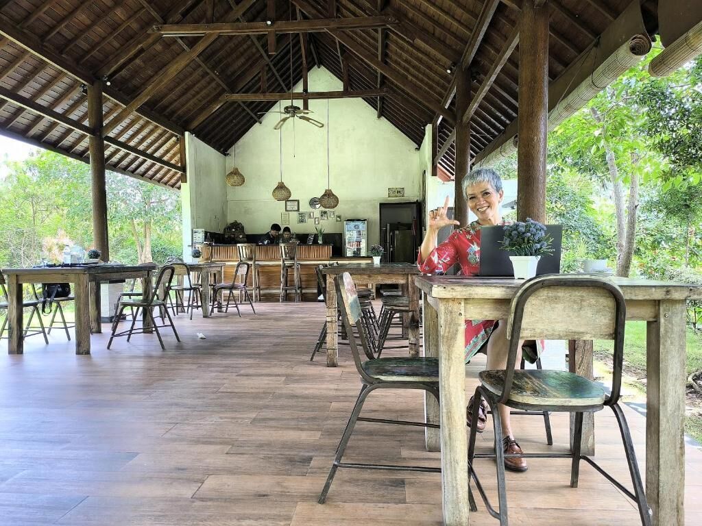 An outdoor dining area with wooden tables and chairs, a bar in the background, and a covered roof structure.