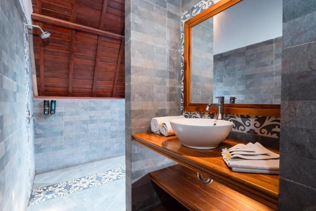 Ein Badezimmer mit Holzboden, einem großen Spiegel, einem weißen Waschbecken und einer Duschkabine.