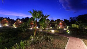 A row of wooden cabins with a paved path leading to them, surrounded by lush greenery. - Tahoma Villas Labuan Bajo by ABM (Labuan Bajo)
