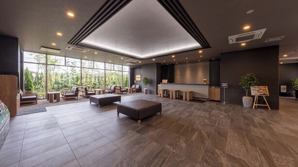 Spaziosa hall con soffitto alto, area relax, reception e ampie finestre che si affacciano sul verde.