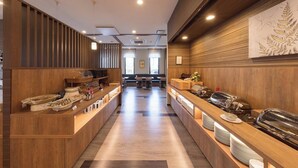 Una moderna hall d'albergo con rivestimenti in legno, una reception e un'area ristorazione con tavoli e sedie.