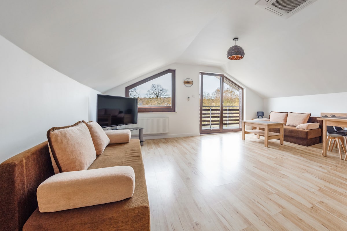 Ein geräumiges Loft mit Holzboden, großem Fernseher, einer Couch, einer Essecke und einem Balkon mit Blick.