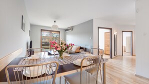 A dining area with a table set for four, a vase with flowers, and a sofa in the background. - Apartamenty Sun & Snow Jasny Brzeg (Wladyslawowo)