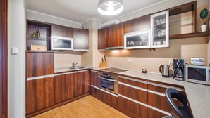 A compact kitchen with wooden cabinets, a built-in oven, a microwave, and a coffee maker. - Apartamenty Sun & Snow Jasny Brzeg (Wladyslawowo)