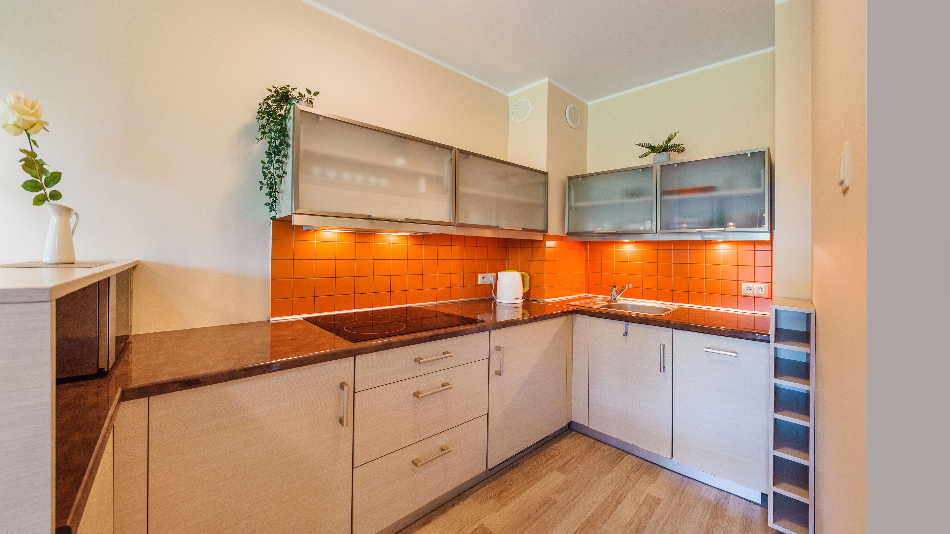 Uma cozinha moderna com armários de madeira, forno embutido e painel de azulejos laranja.