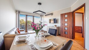 A dining area with a table set for two, a sofa, and a balcony with a view. - Apartamenty Sun & Snow Jasny Brzeg (Wladyslawowo)