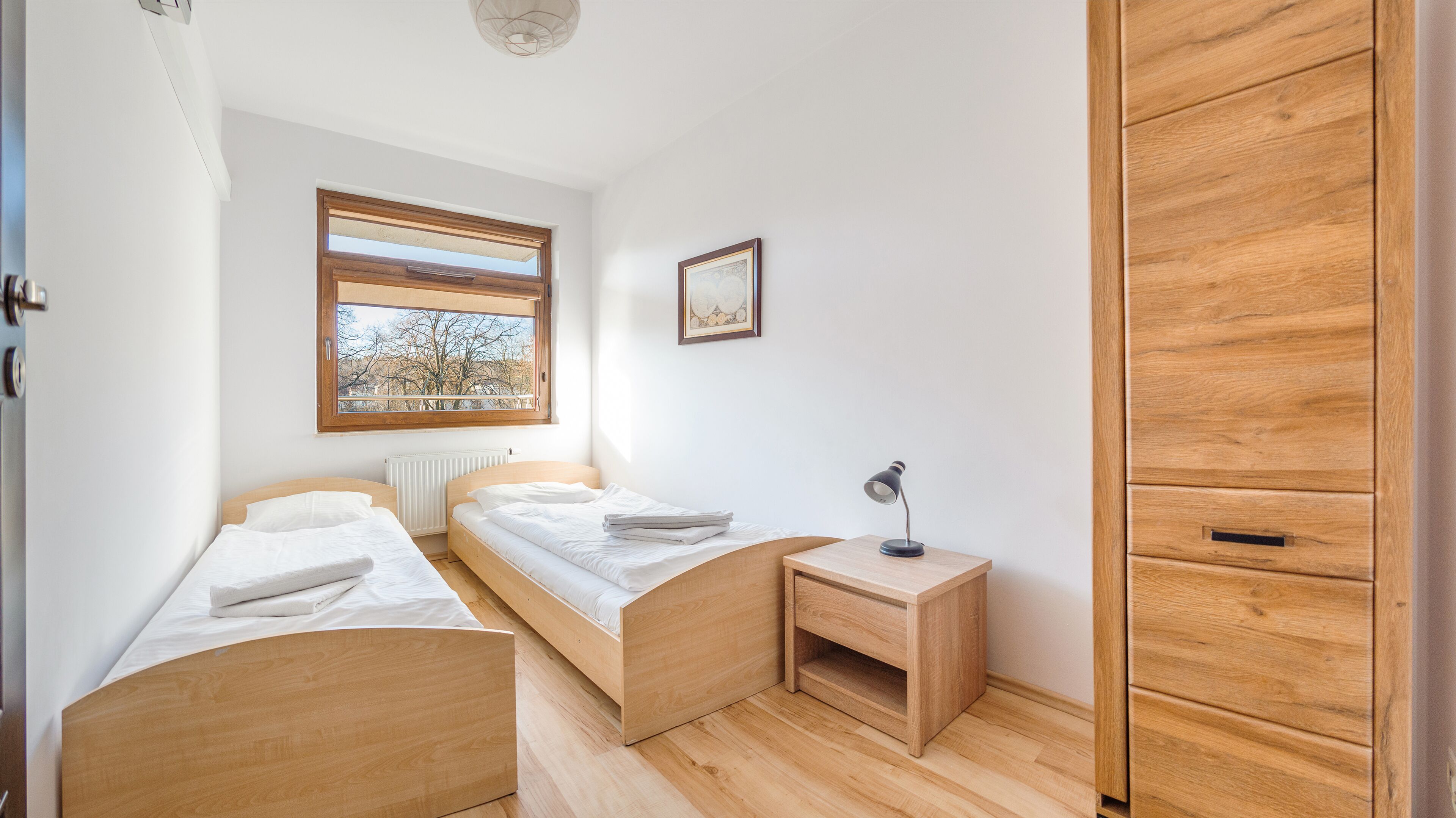 A small, tidy room with two wooden beds, a desk, a radiator, and a wardrobe.