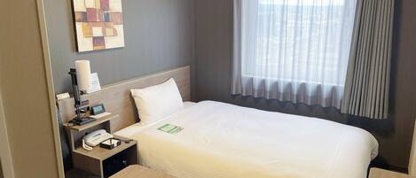 Une chambre d’hôtel avec un lit, une table de chevet, une lampe et une fenêtre avec des rideaux.