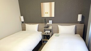 A hotel room with two single beds, a bedside table with a phone and a lamp, and a wall clock.