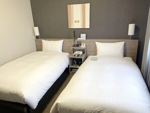A hotel room with two single beds, a bedside table with a phone and a lamp, and a wall clock.