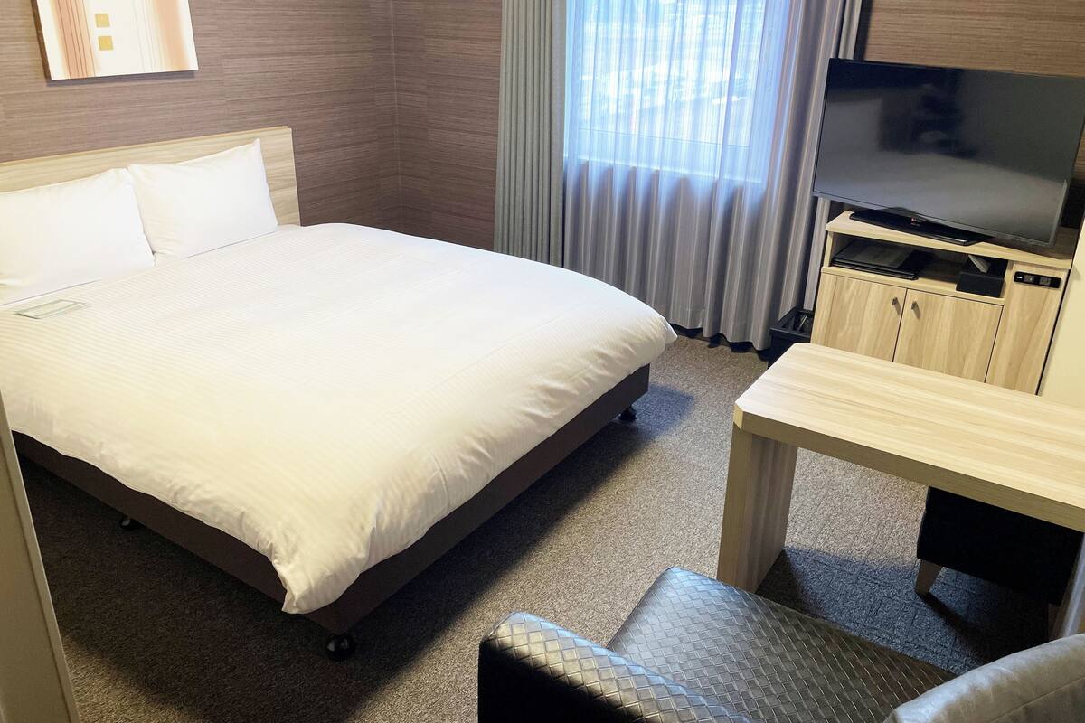A hotel room with a large bed, a TV on a wooden stand, and a window with curtains.