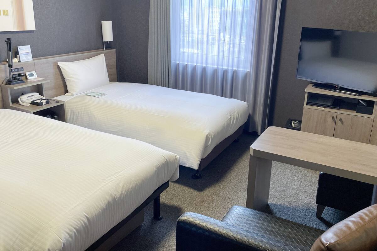 A hotel room with two beds, a desk, a television, and a nightstand with a phone and a lamp.