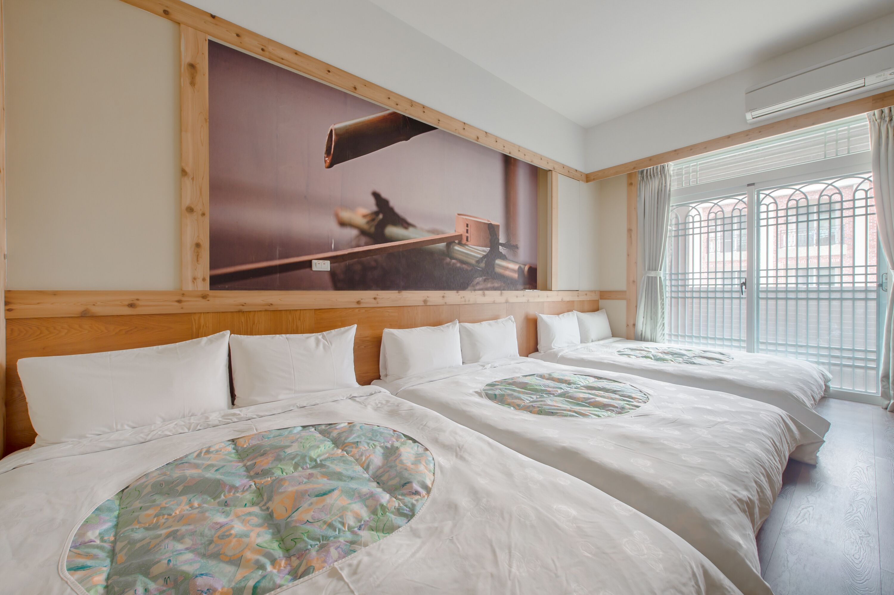 Quarto de hotel com duas camas, um mural grande na parede e uma janela com grades de metal.