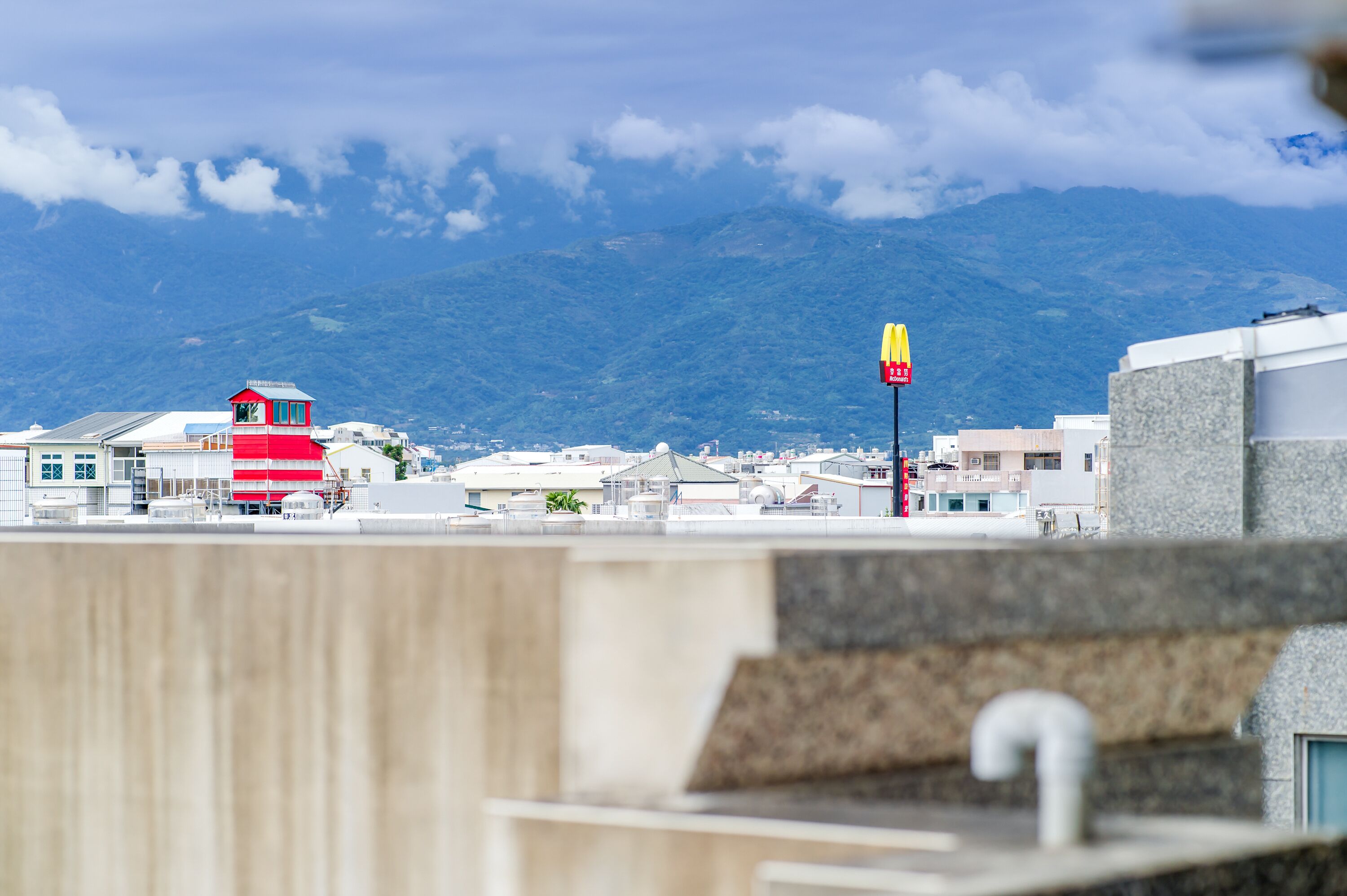 A view of a coastal town with a prominent red and white building, a McDonald's sign, and a mountain in the background.