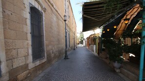 A narrow cobblestone street with stone buildings on either side, a covered walkway with plants, and a metal fence. - Gabriel Apartments - Stylish Suites - King George ST (Jerusalem)