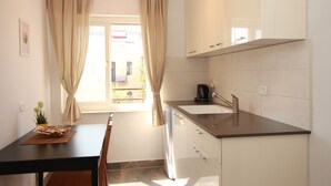 A kitchen with a black countertop, white cabinets, a sink, and a window with curtains. - Gabriel Apartments - Stylish Suites - King George ST (Jerusalem)