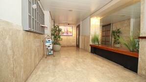 A hallway with marble flooring, a reception desk, a large potted plant, and a wall-mounted security camera. - Gabriel Apartments - Stylish Suites - King George ST (Jerusalem)
