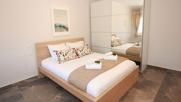 A neatly made bed with a wooden headboard, a large mirror, and a framed picture on the wall. - Gabriel Apartments - Stylish Suites - King George ST (Jerusalem)