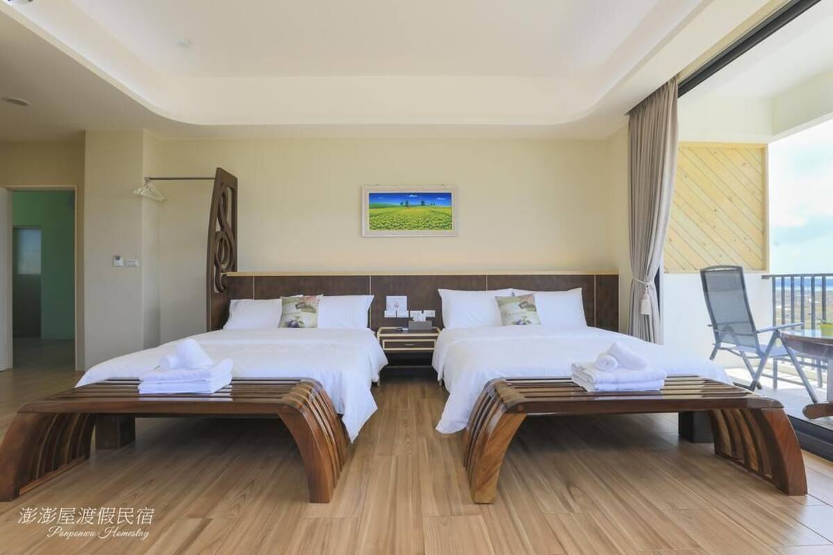 A hotel room with two beds, a wooden floor, a painting on the wall, and a balcony with chairs.