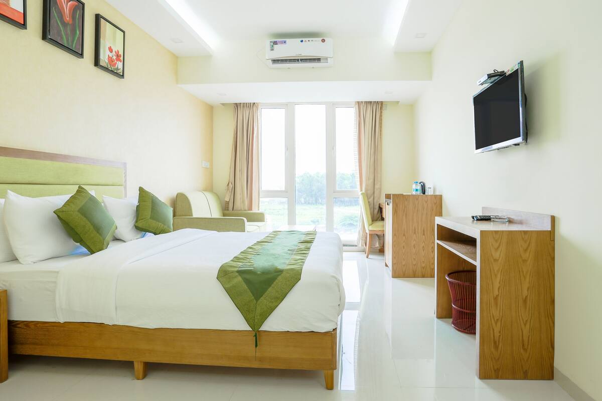 A hotel room with a bed, a desk, a TV, and a window with curtains.