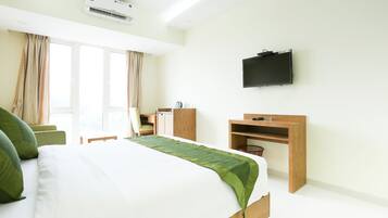 Una habitación de hotel con cama, escritorio, televisor y ventana con cortinas.