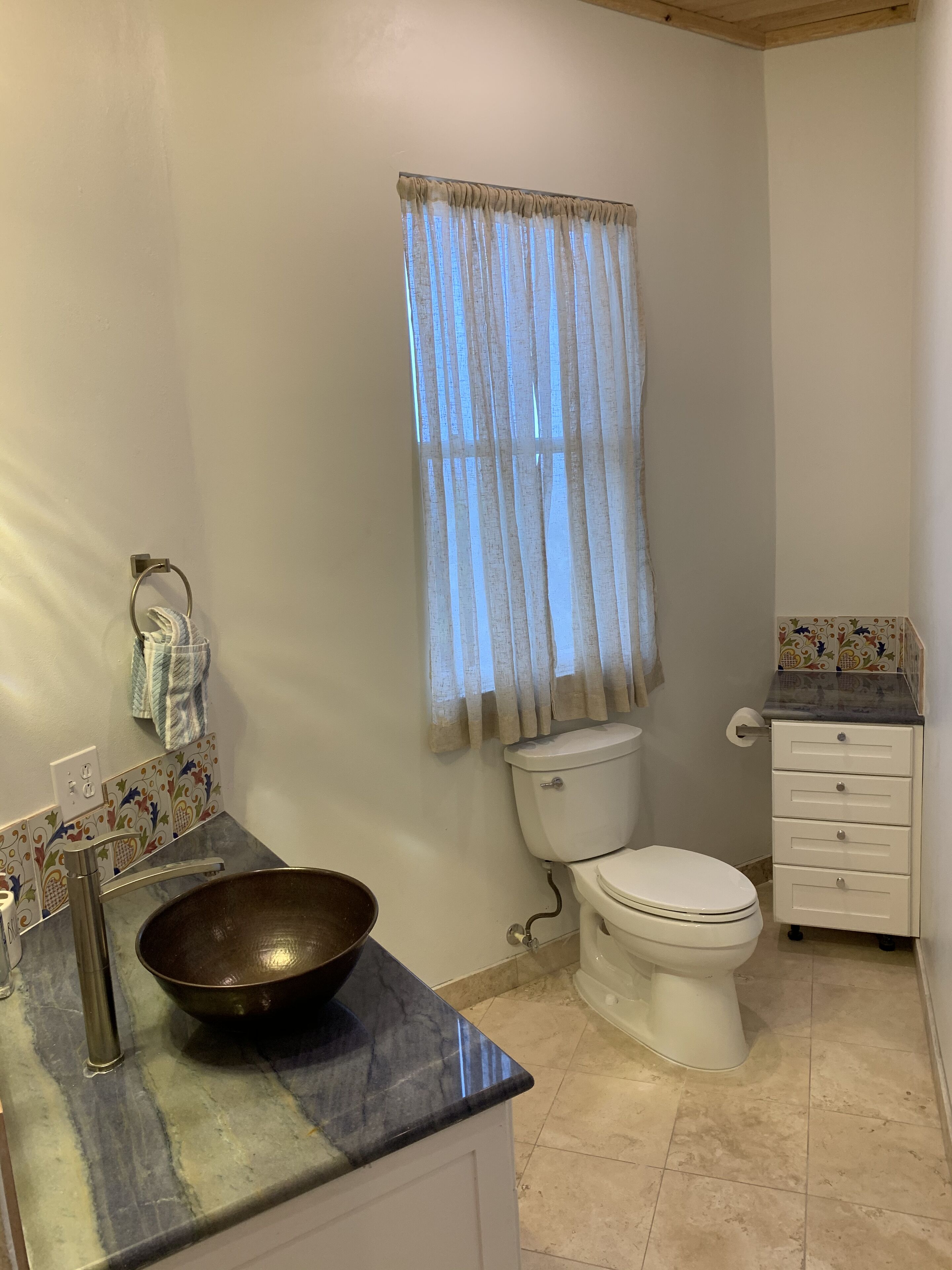 A bathroom with a toilet, sink with a large basin, a towel rack, and a cabinet with drawers.
