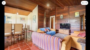 Una habitación acogedora con paredes y techo de madera, un sofá, un televisor y una zona de comedor con sillas y una mesa.