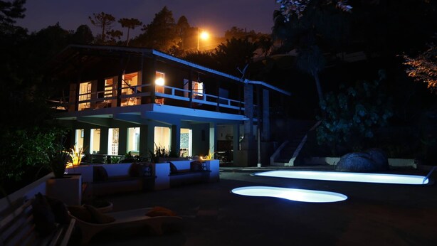 Una casa de dos pisos con balcón, piscina e iluminación exterior.