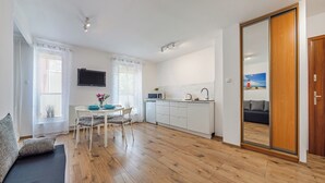 A modern kitchen with white cabinets, a microwave, and a sink. There is a dining table with chairs and a TV mounted on the wall.
