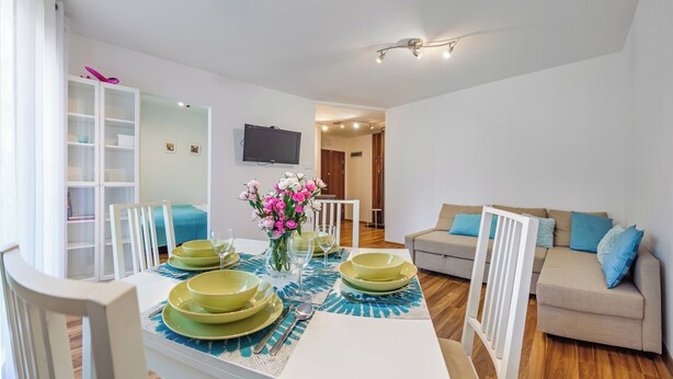 A dining area with a table set for four, a sofa, and a TV mounted on the wall.