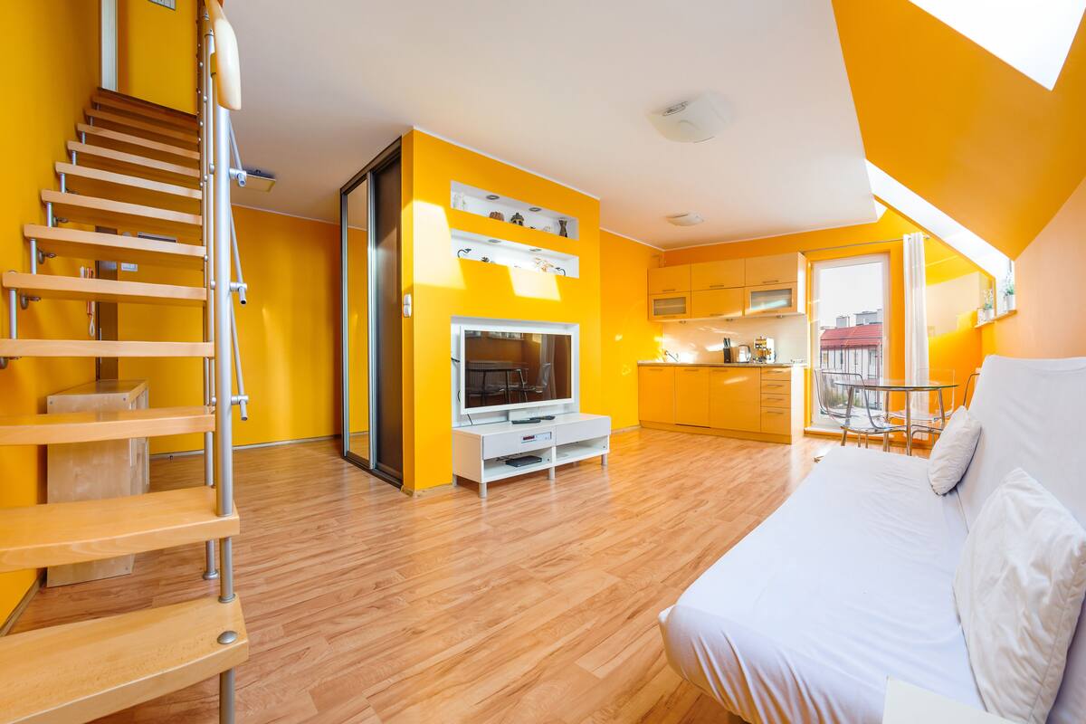 A modern apartment with a wooden staircase, a TV, a bed, and a kitchen area.