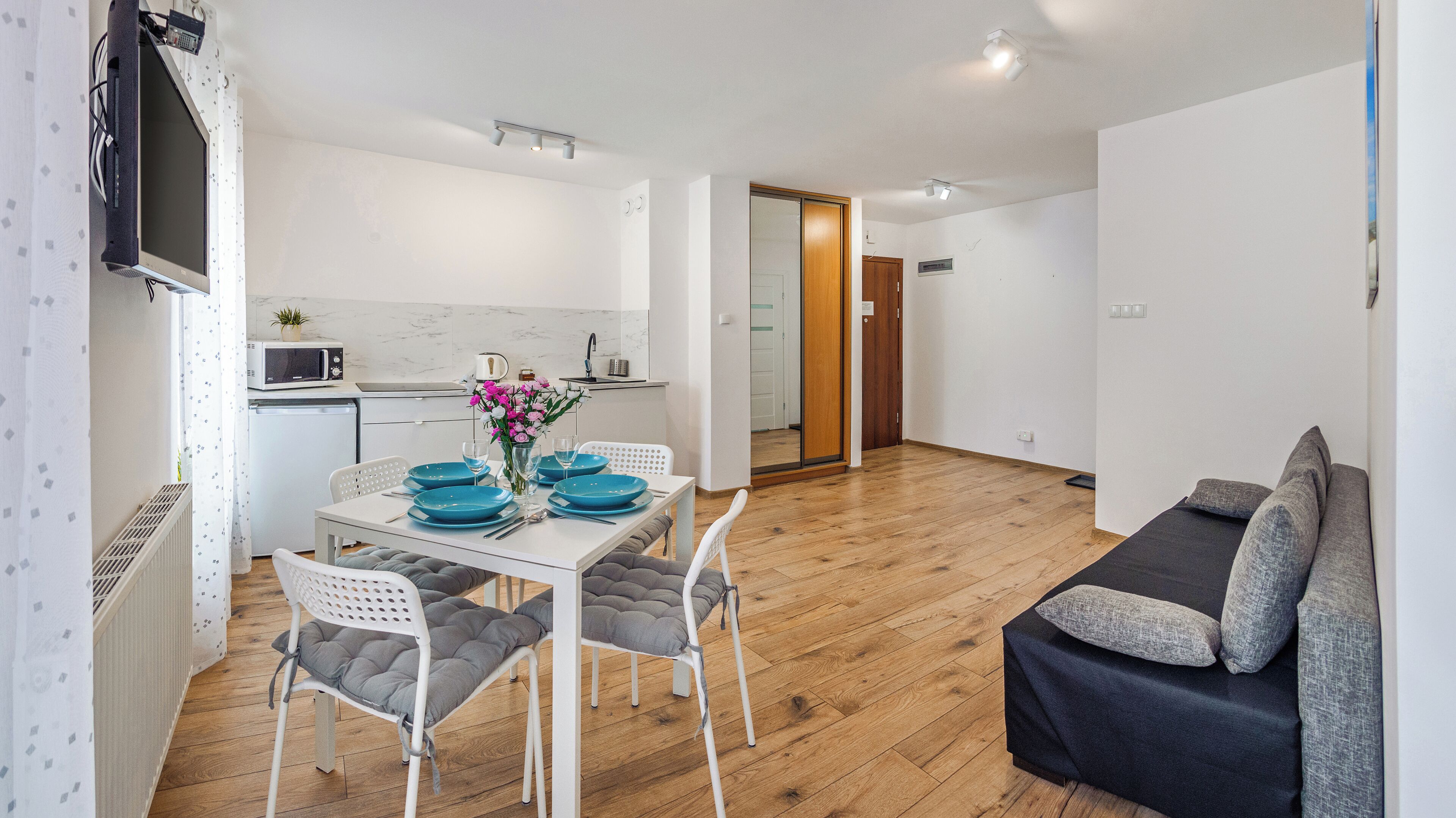 A modern living space with a dining area, kitchenette, and a sofa.