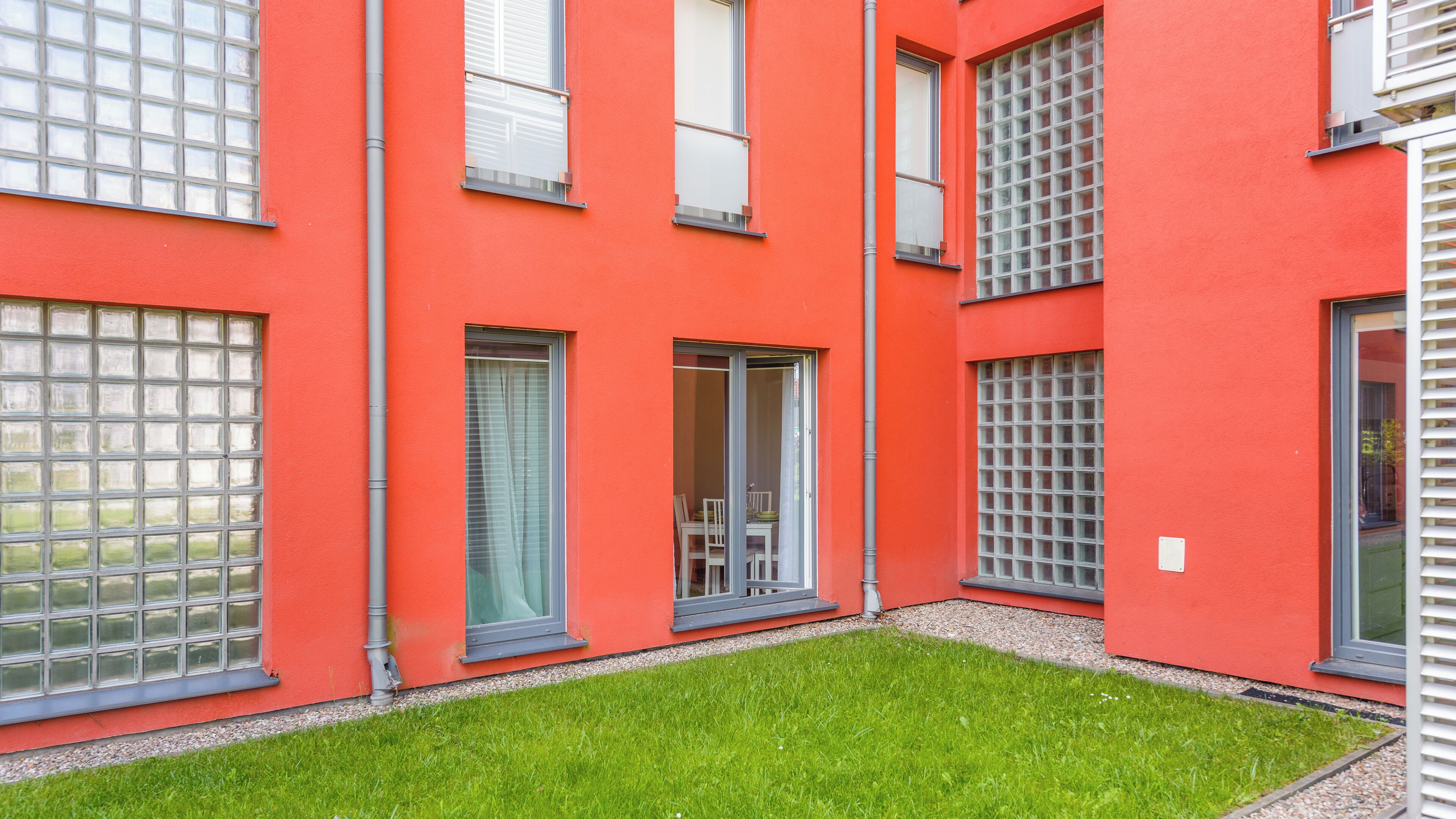 A red building with multiple windows and a small grassy area in front.