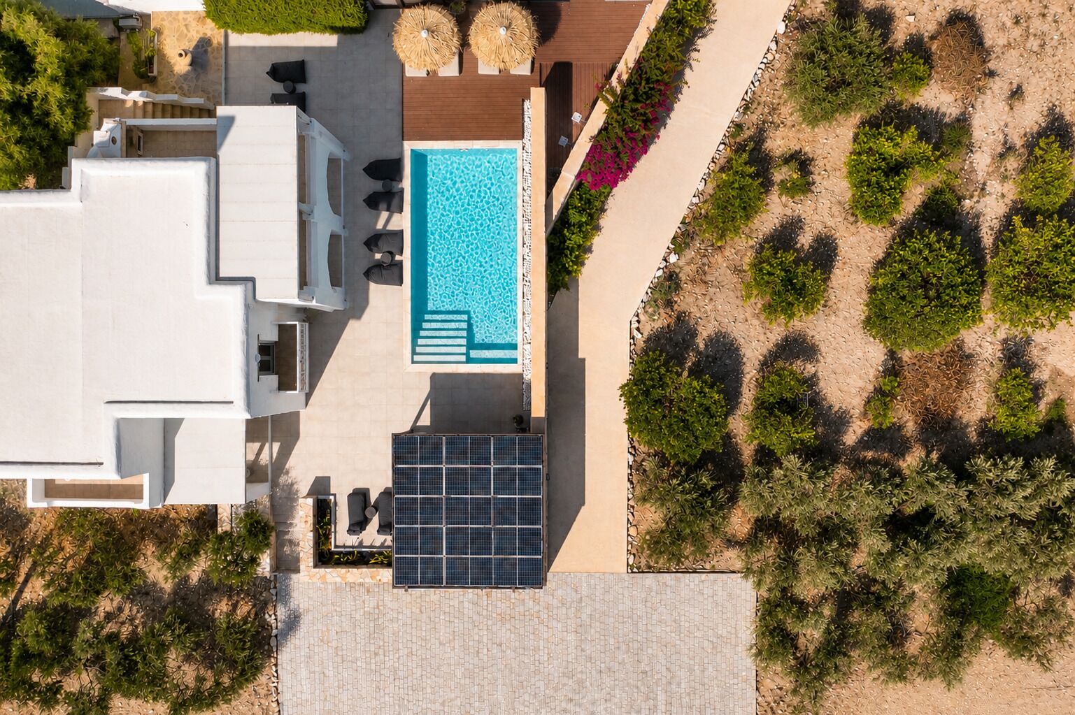 Vue aérienne d’un complexe hôtelier moderne doté d’une piscine, de chaises longues et d’une installation de panneaux solaires.