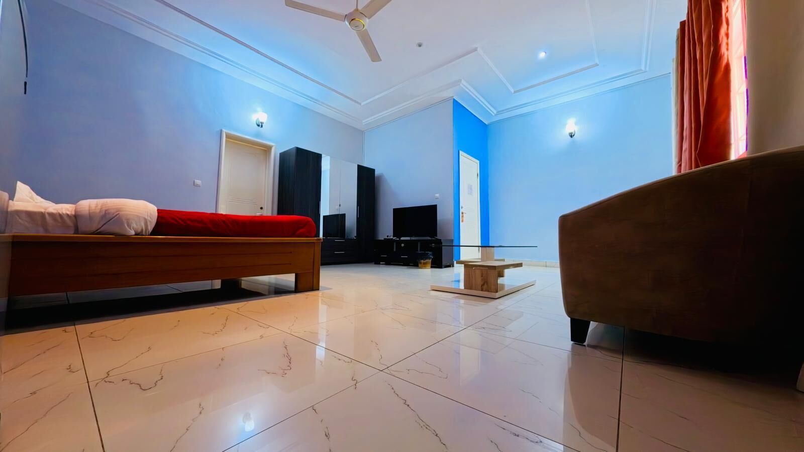 Quarto de hotel moderno com cama, sofá, televisão e uma mesinha.