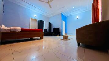 Quarto de hotel moderno com cama, sofá, televisão e uma mesinha.