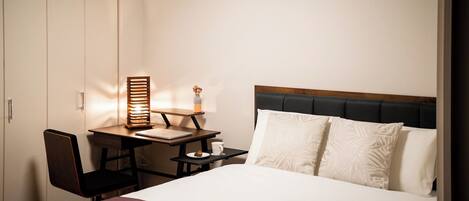 A hotel room with a bed, a desk with a chair, a nightstand, and a wardrobe.