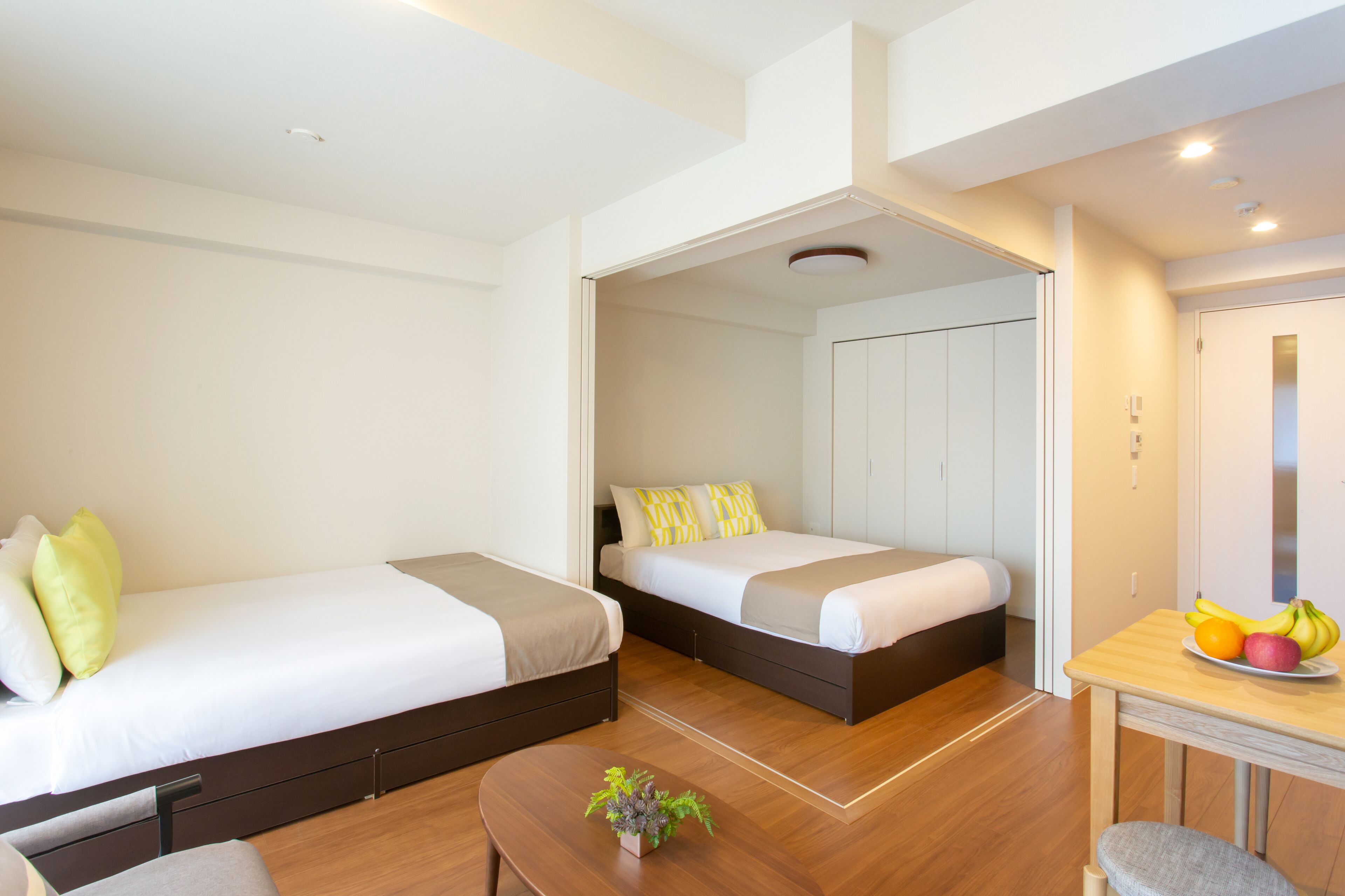 Habitación de hotel moderna con dos camas, una mesita con fruta y una planta.