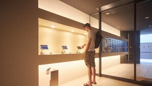 Un homme se tient dans le hall d’un hôtel moderne, où l’on aperçoit un comptoir d’accueil, des bornes d’enregistrement numérique et une cloison en verre.