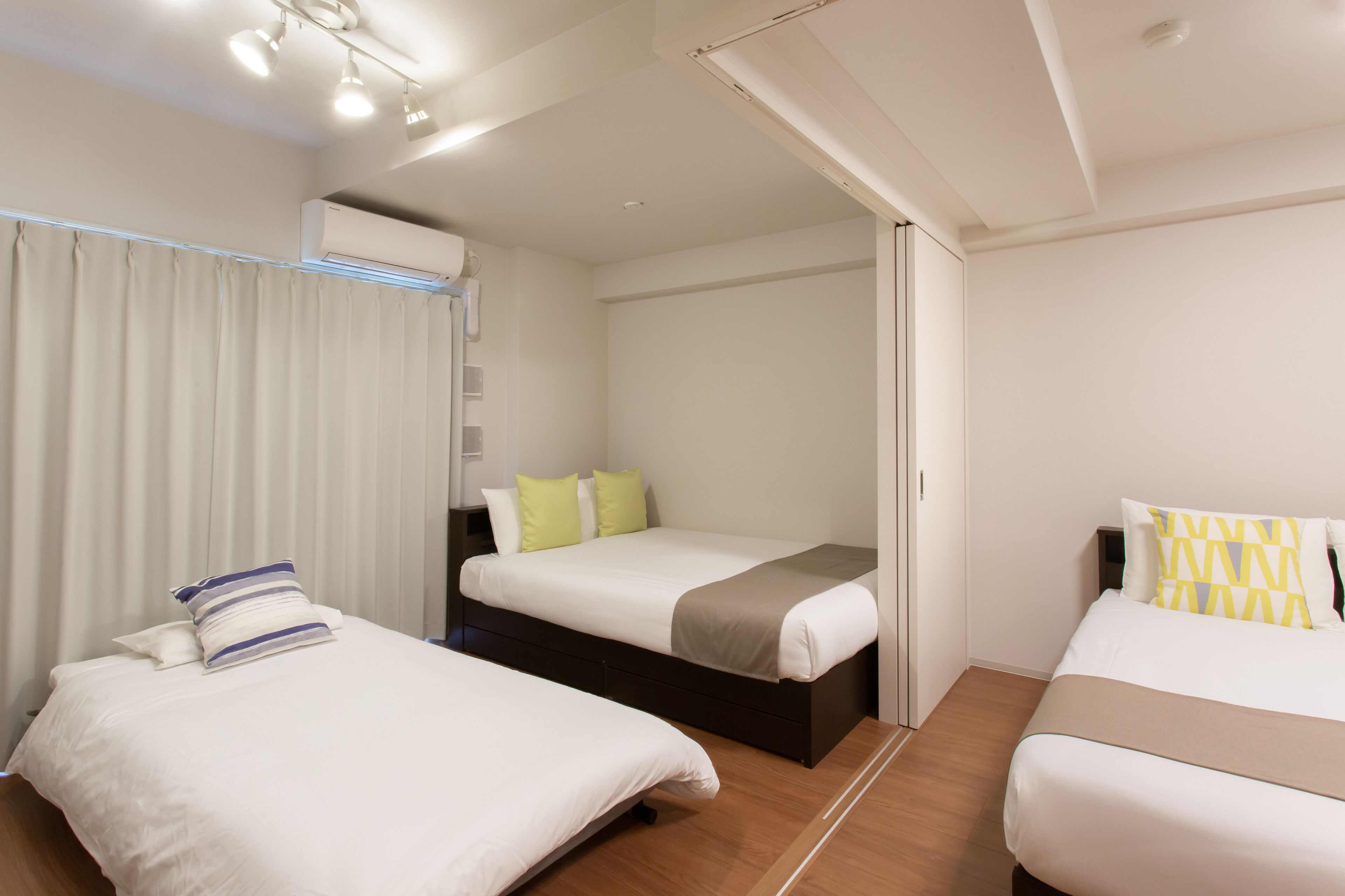 Une chambre d’hôtel avec deux lits, un plancher en bois, une fenêtre avec des rideaux et un appareil de climatisation.