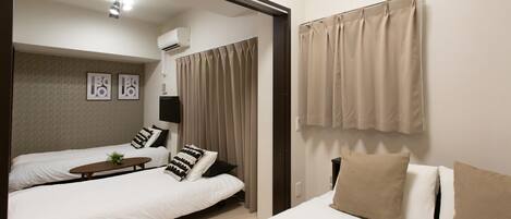 A hotel room with two beds, a small table, and a window with curtains.