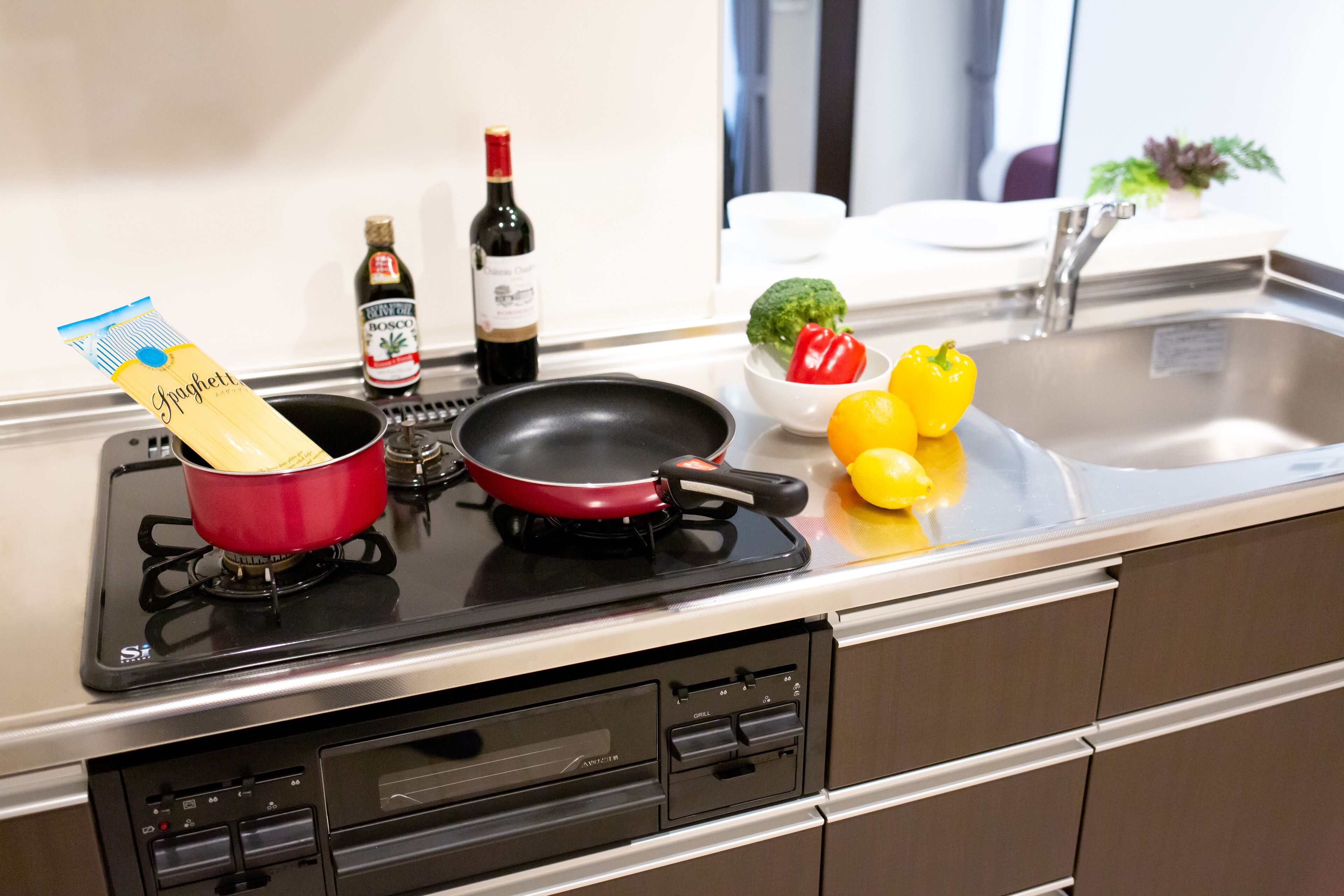 A kitchen with a stove, a frying pan, a pot, a bottle of wine, and some vegetables.