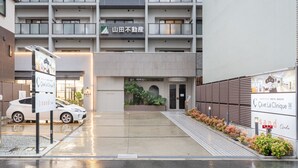 Un immeuble à plusieurs étages avec un espace de stationnement devant. On y voit des panneaux indiquant « Café La Clinique » et « 8 sand ».