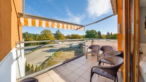 Un balcon avec des fauteuils en osier, une balustrade en verre et une vue sur un parking et des arbres.