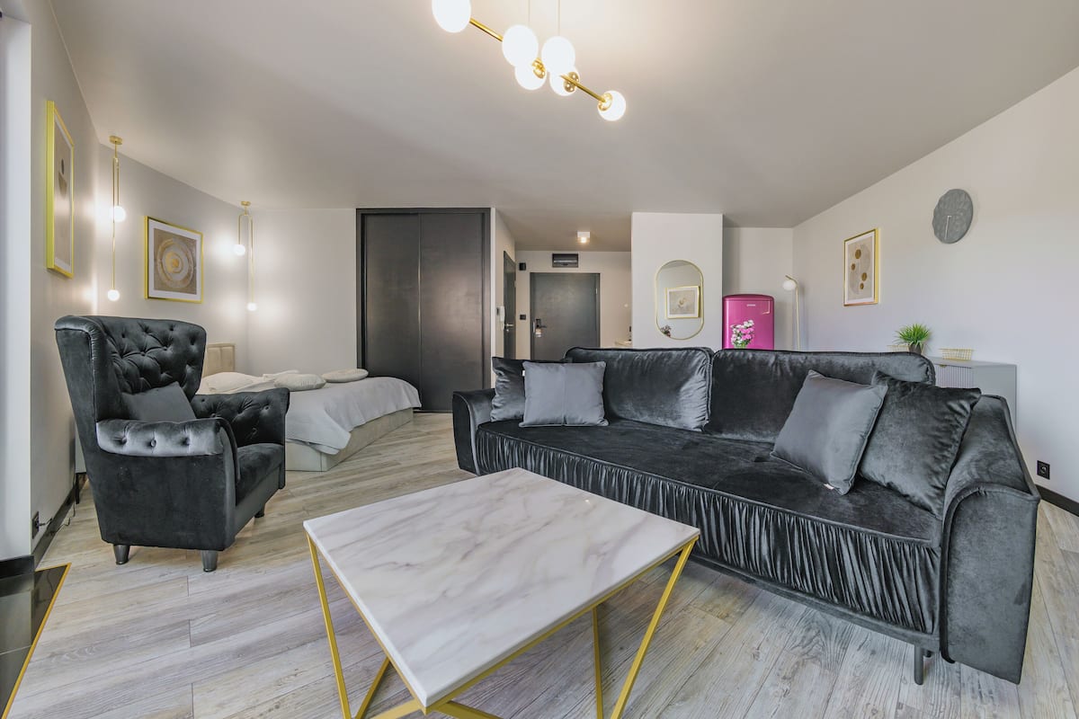 A modern living room with a black sofa, a tufted armchair, and a marble coffee table.